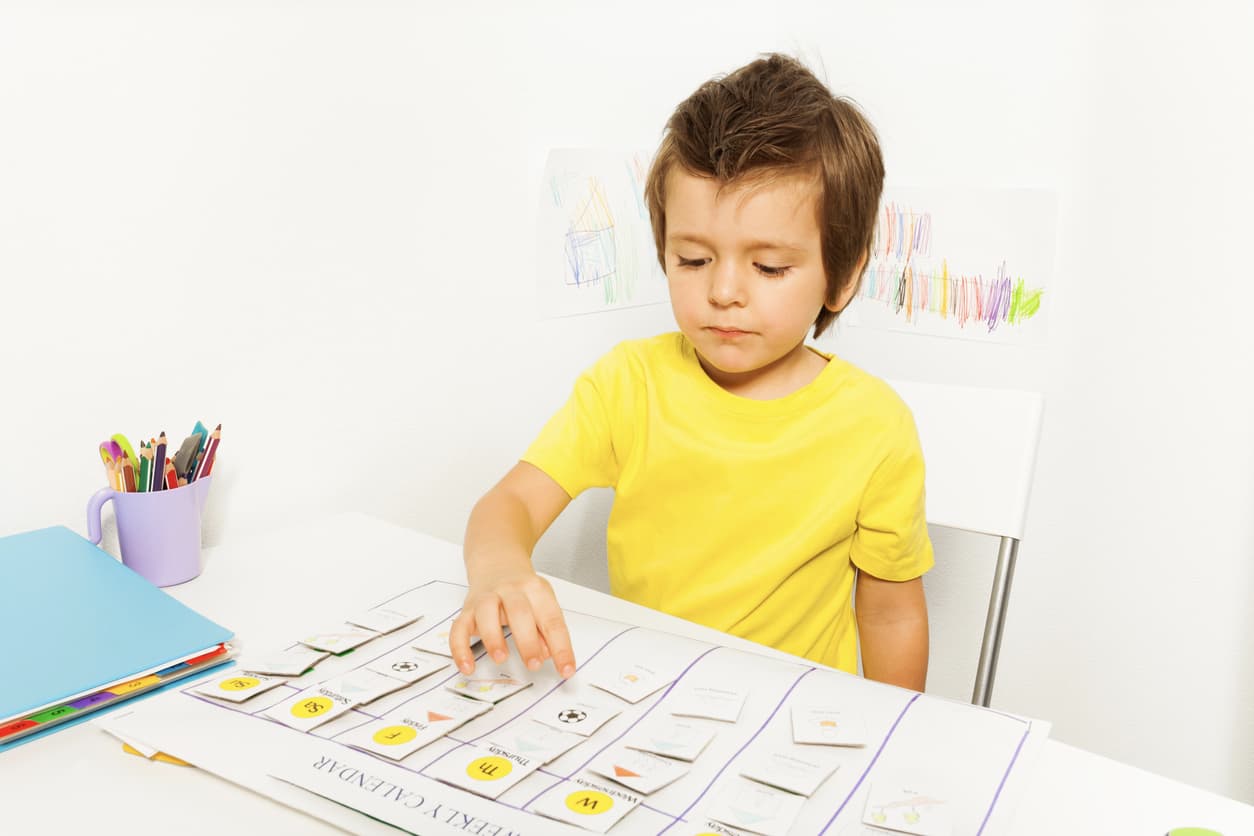 boy in yellow shirt plays in developing game pointing at calendar during ABA sitting at the table