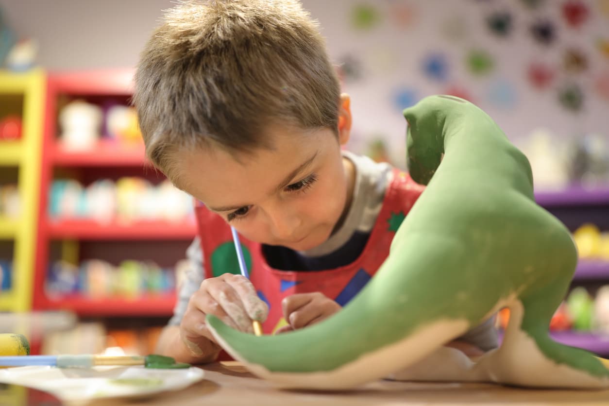 A child focuses on art activities with a model dinosaur